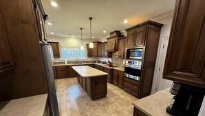 A spacious kitchen with dark wooden cabinets, a central island, stainless steel appliances, and a large window providing natural light. - Escape to Tranquility 125 Acre Property with Trails Lake Spacious House Fire Pit (Kingsland)