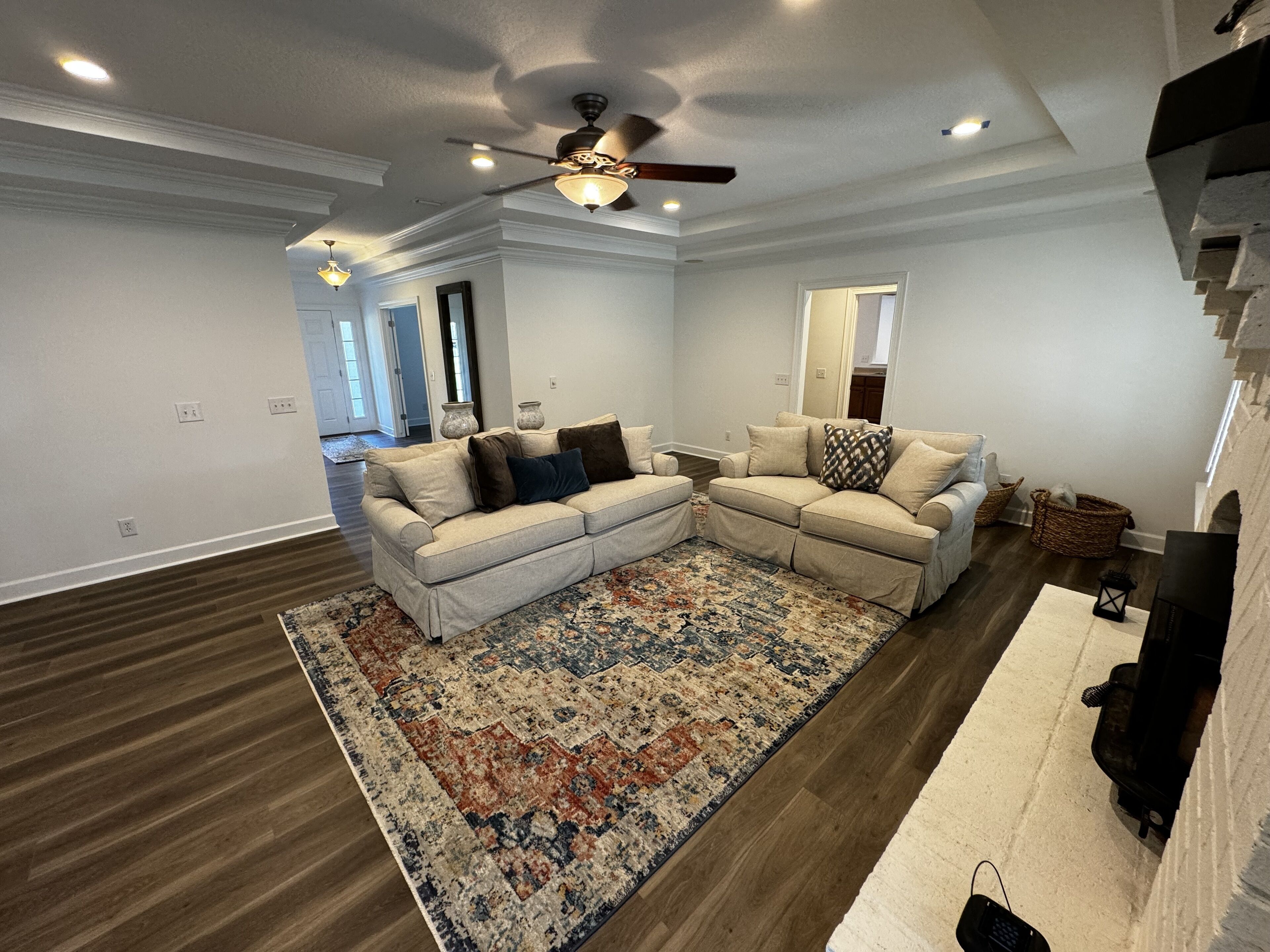 Ein geräumiges Wohnzimmer mit einem beigefarbenen Ecksofa, einem gemusterten Teppich und einem Deckenventilator.