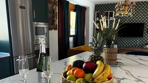 A marble countertop with a fruit basket, two wine glasses, and a bottle of wine.