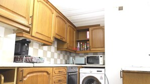 Uma cozinha compacta com armários de madeira, micro-ondas, cafeteira e máquina de lavar roupa.