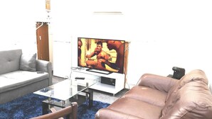 Uma sala de estar com televisão de tela plana, sofá, mesa de centro de vidro e poltrona de couro.