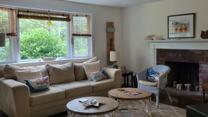 Ein Wohnzimmer mit einem beigefarbenen Sofa, zwei runden Couchtischen, einem Korbstuhl und einem Kamin.