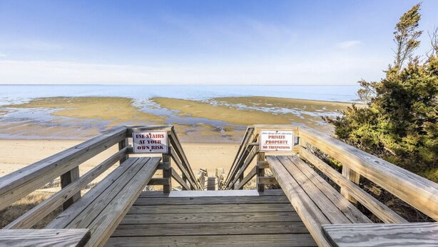 Eine Holztreppe führt zu einem Strand, mit Schildern, die vor privatem Eigentum warnen und das Betreten verbieten.