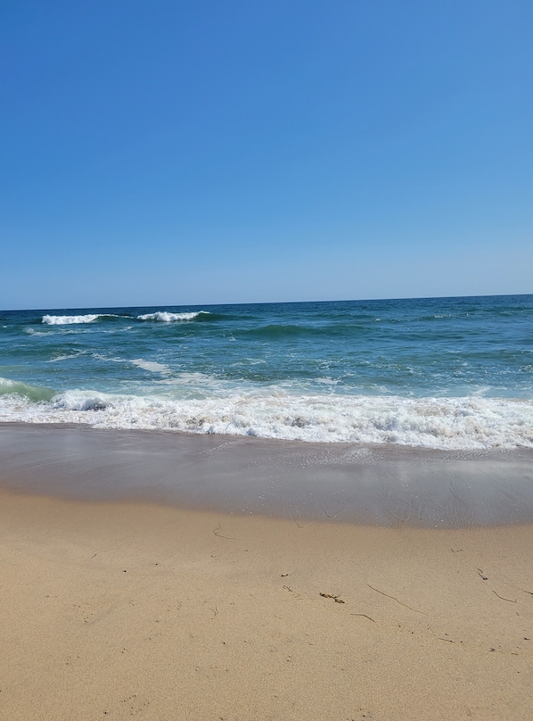 Une plage où les vagues se brisent près du rivage, sous un ciel dégagé.