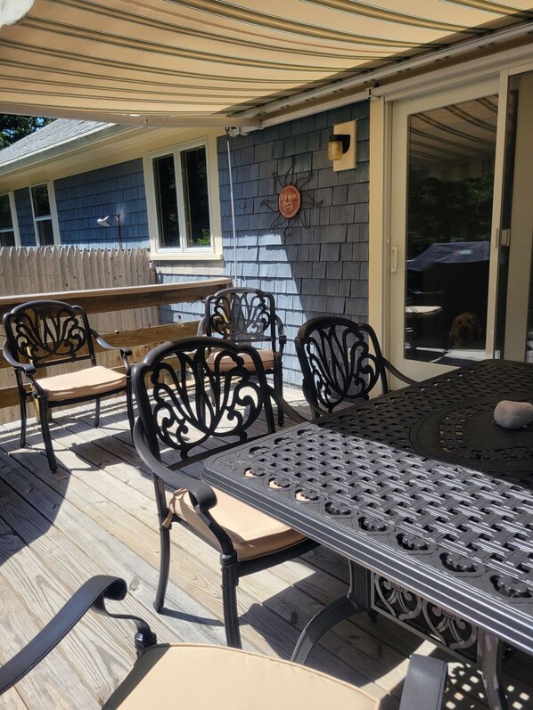 Um pátio externo com mesa e cadeiras, um deck de madeira e uma área coberta com vista para a casa.