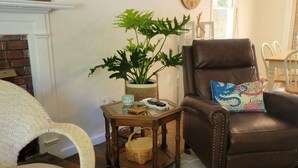 Ein Wohnzimmer mit einem braunen Ledersessel, einem Korbstuhl, einem Holztisch und einem Blumentopf.