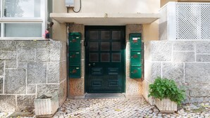 Entrada de un edificio con una puerta verde, dos buzones verdes y una planta en maceta.