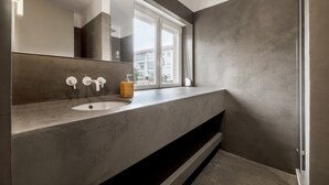 Un baño moderno con un espejo grande, un lavamanos y una ventana.