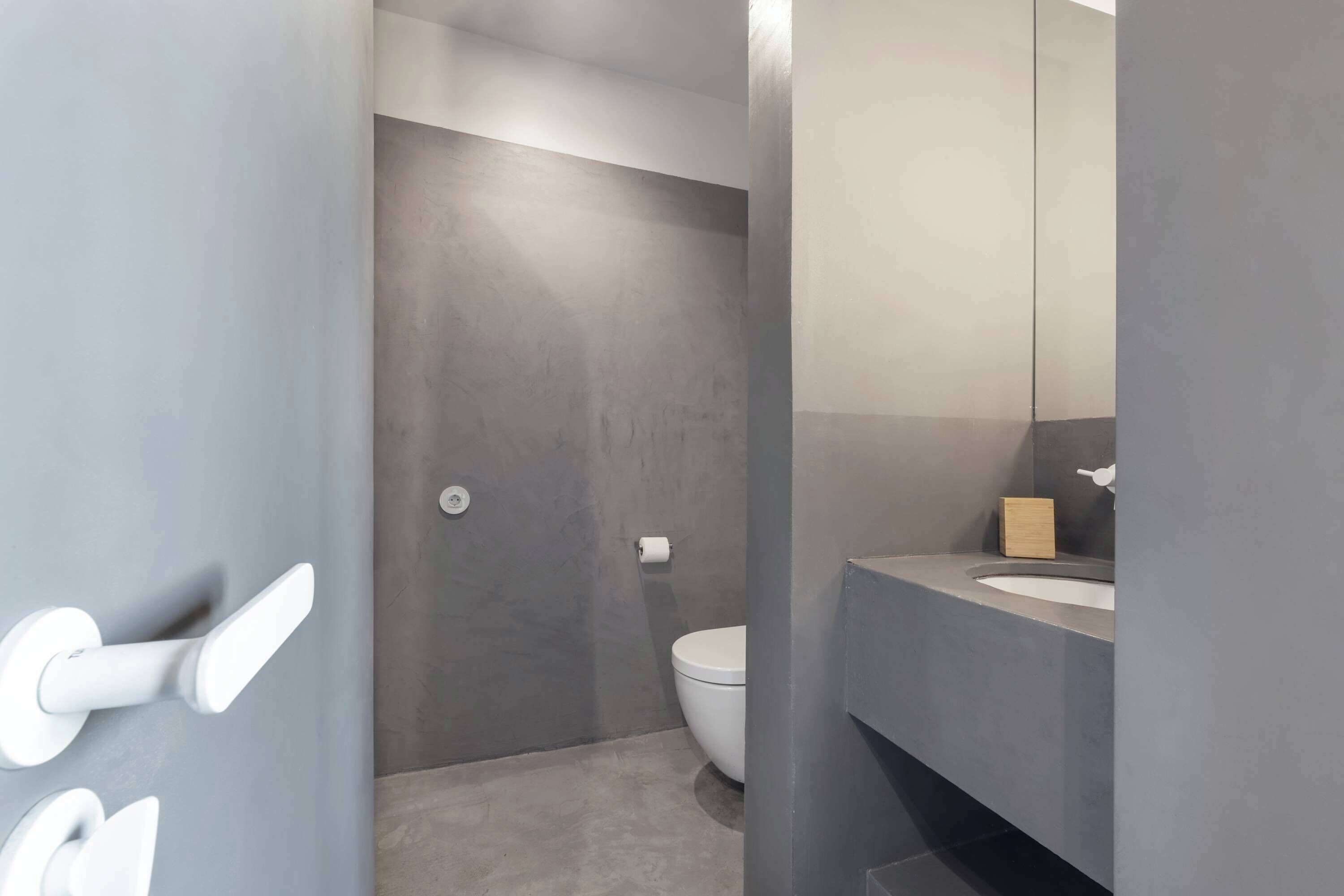 A modern bathroom with a grey wall, a white toilet, and a sink with a mirror.