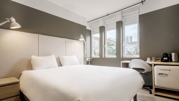 Una habitación de hotel moderna con una cama grande, mesitas de noche, un escritorio y una silla.