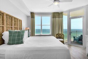Une chambre avec un grand lit, une vue sur l’océan par une porte-fenêtre coulissante et un ventilateur de plafond.
