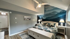 Une chambre à coucher comprenant un lit, des tables de chevet, une commode, un ventilateur de plafond et une fresque murale.