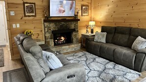 Un salon chaleureux avec une cheminée en pierre, des canapés en cuir et un téléviseur fixé au-dessus.