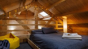 Une chambre mansardée chaleureuse, avec un lit, un fauteuil poire et des guirlandes lumineuses.