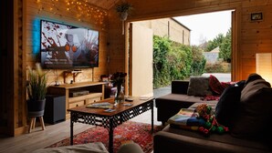 Un salon chaleureux avec un téléviseur à écran plat, des meubles en bois, un tapis rouge et une vue sur le jardin.