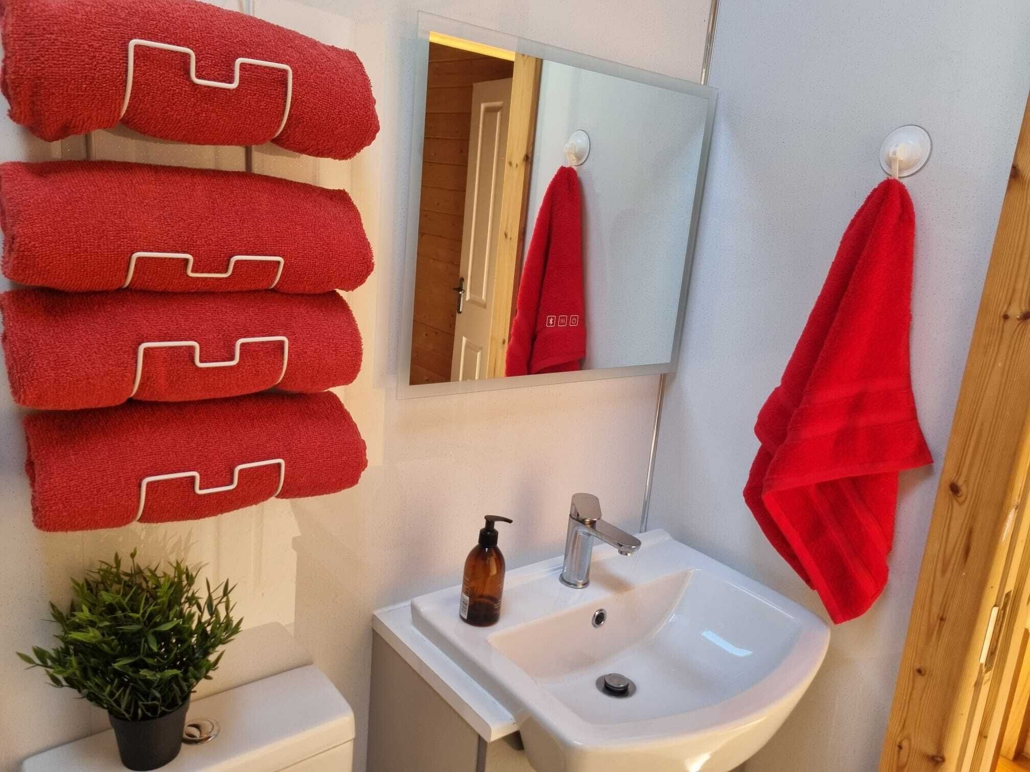 Une salle de bain avec un lavabo blanc, un miroir et un porte-serviettes rouge sur lequel sont disposés plusieurs serviettes.