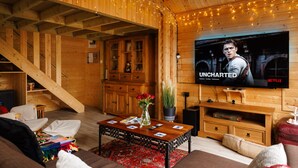 L’intérieur d’un chalet en bois chaleureux et accueillant, avec un téléviseur diffusant la série « Uncharted » sur Netflix, un escalier, des meubles en bois et un coin salon confortable.