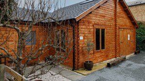 Une cabane en bois avec un toit en pente, une petite véranda et un pot de fleurs.