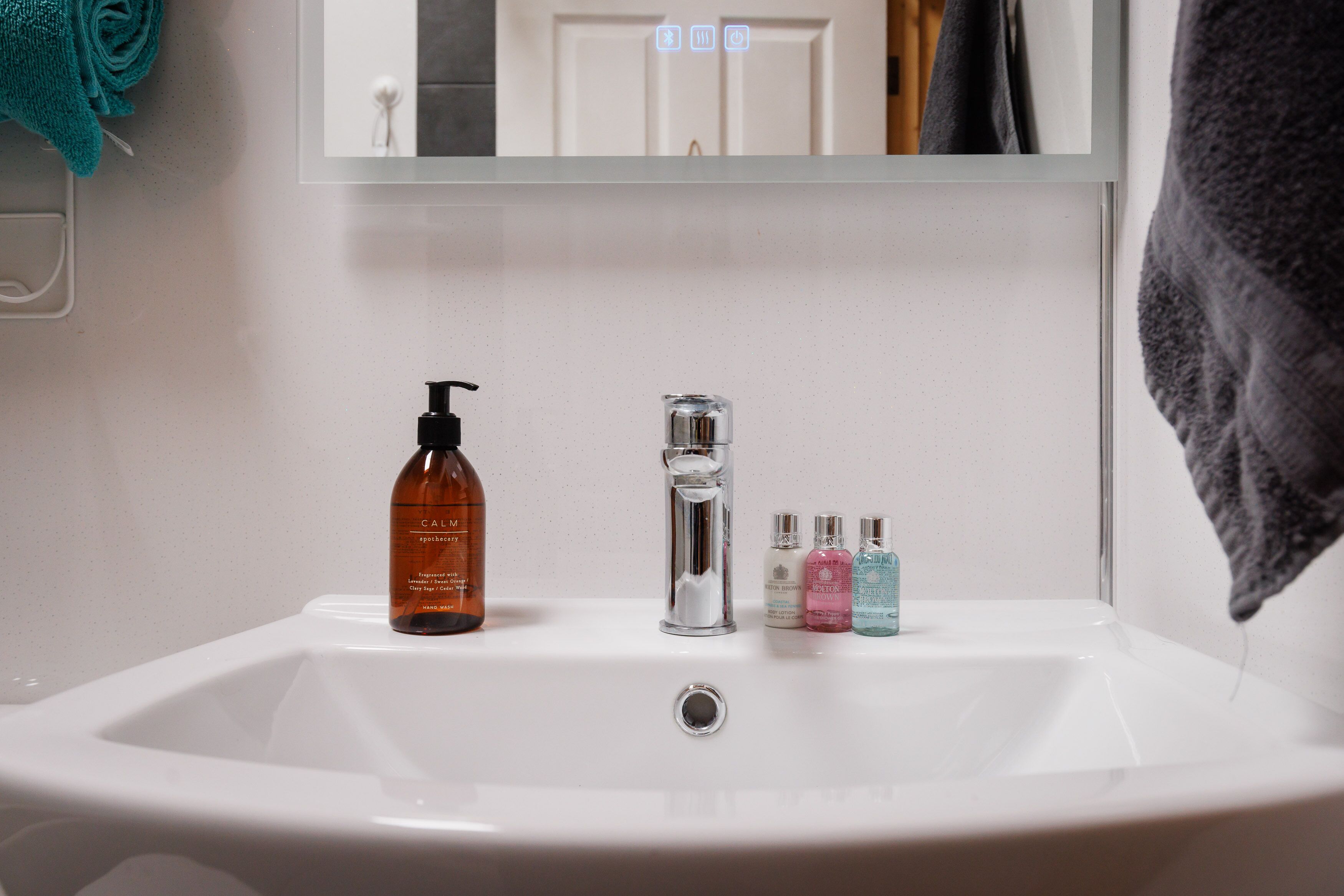 A bathroom sink with a mirror above it, a faucet, and three bottles of liquid soap.