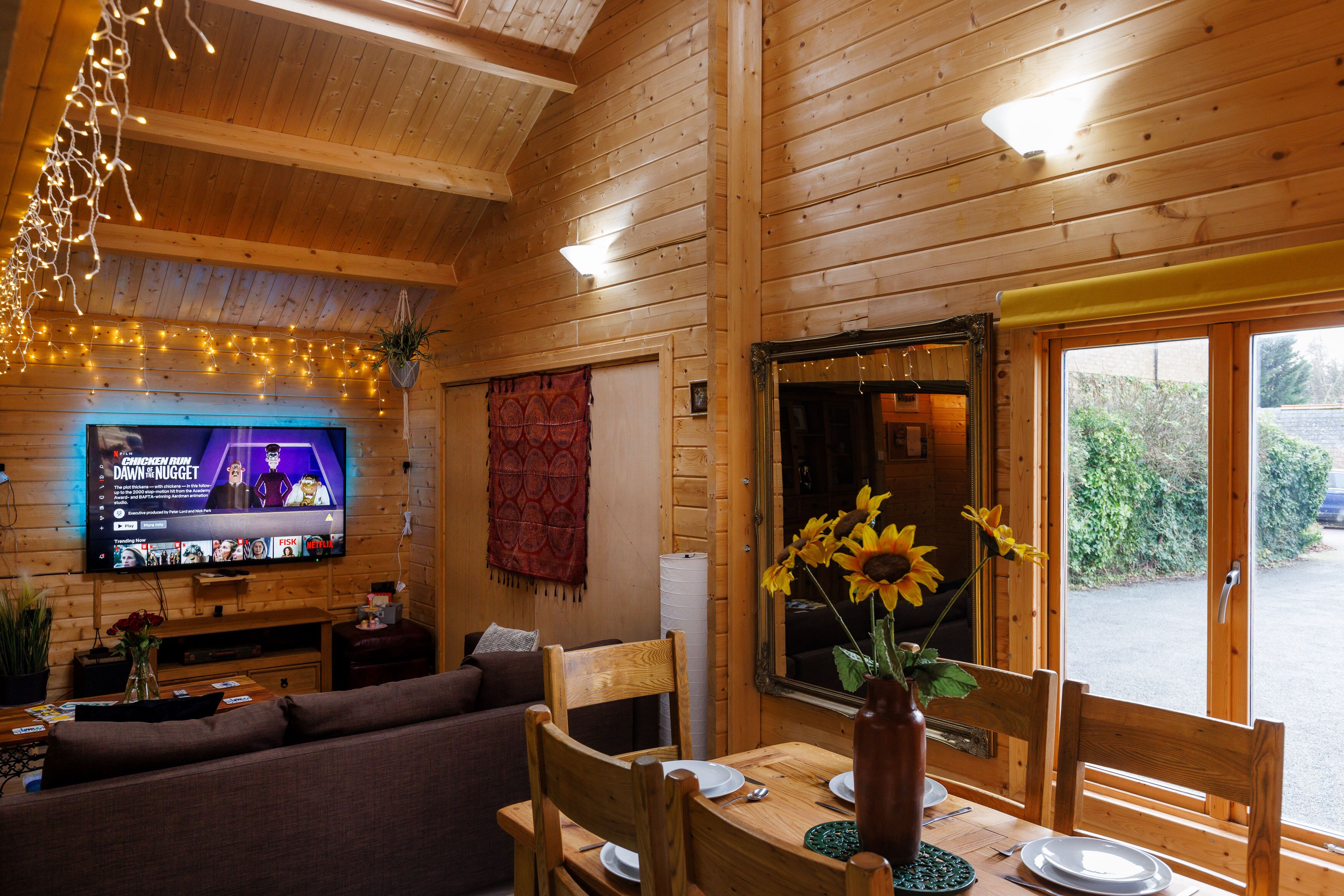 L’intérieur d’un chalet en bois est aménagé avec un téléviseur, des meubles en bois et une fenêtre donnant sur un paysage verdoyant.