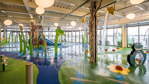 Zona de juegos interior con fuente de agua, toboganes y estructuras de juego coloridas.