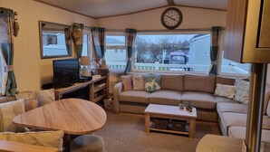 Un interior de autocaravana acogedor con un sofá, un televisor, una mesa de comedor y un reloj en la pared.