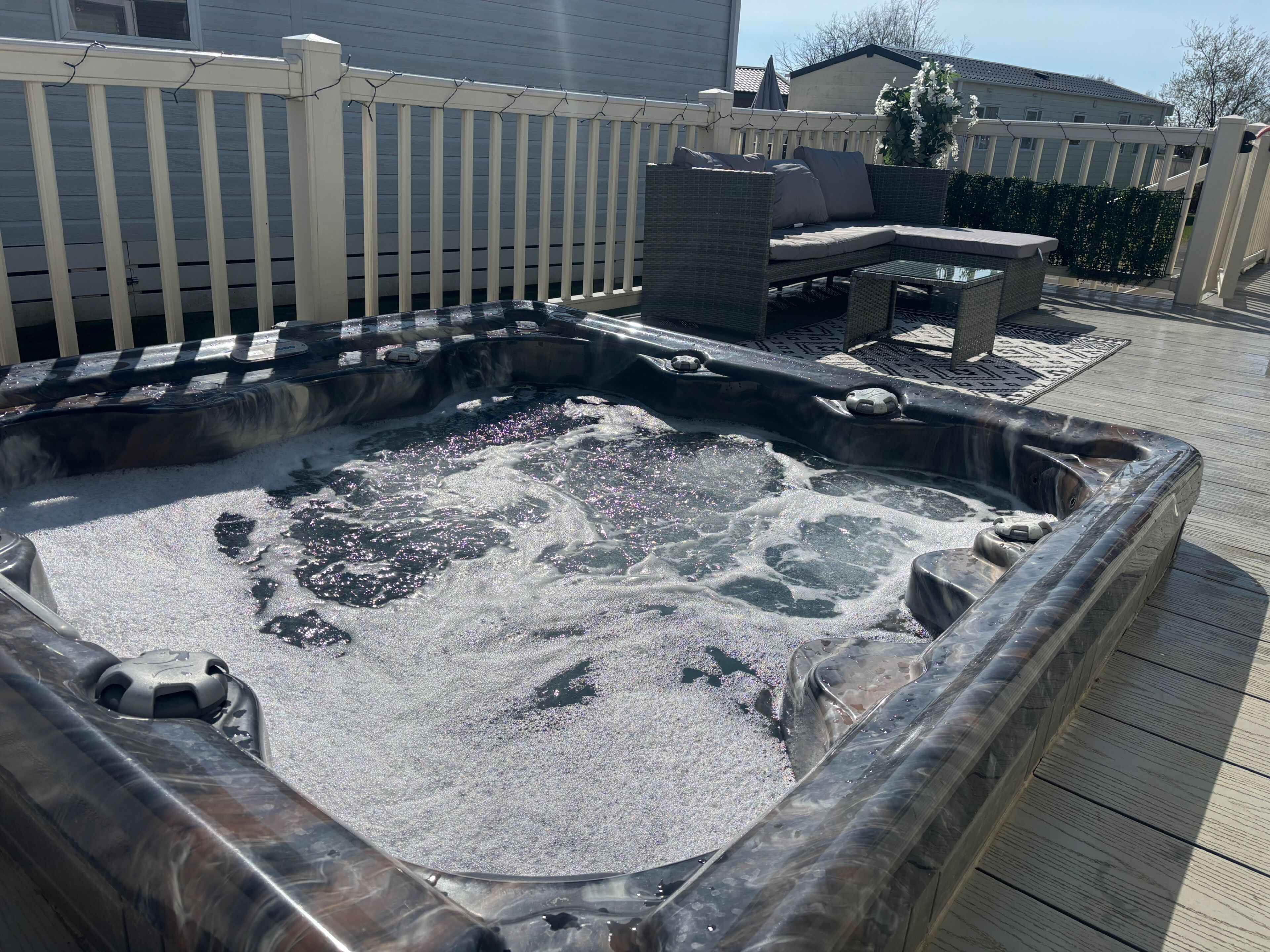 Un bain à remous avec une terrasse en bois et une clôture blanche.