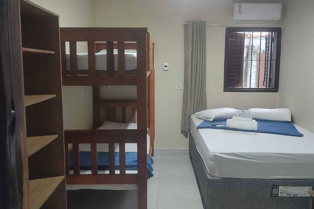 A bedroom with a bunk bed, a single bed, a wardrobe, and a window with bars.