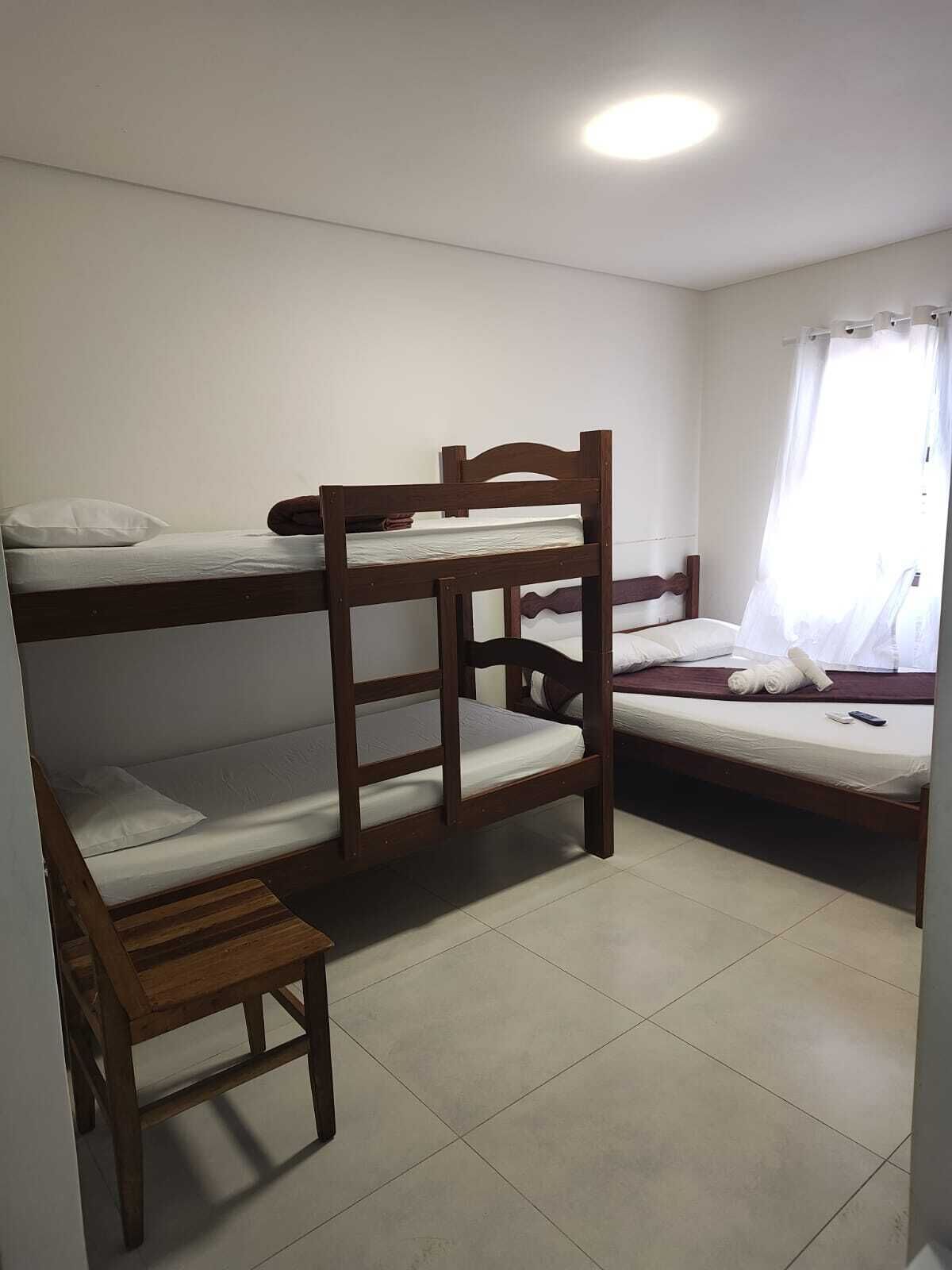 A dormitory room with bunk beds, a wooden bench, and a single bed with a curtain.
