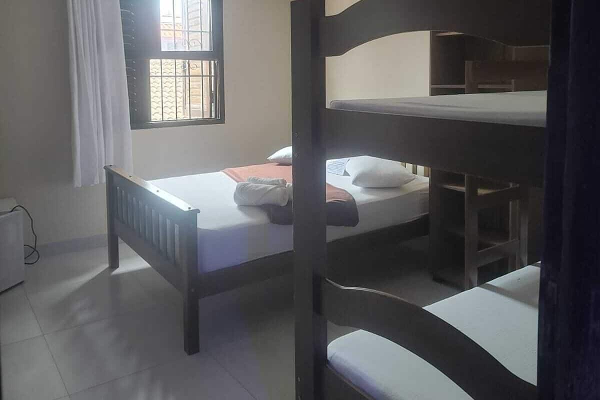 A dormitory room with bunk beds, a window with bars, an air conditioning unit, and a radiator.