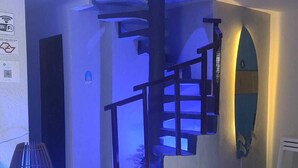 A modern interior with a spiral staircase, a large decorative vase, and a surfboard decoration. - Pousada Kasarão Praia Grande (Ubatuba)