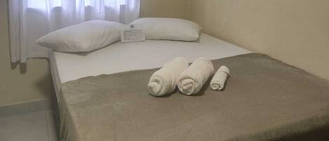 Ein Hotelzimmer mit Bett, weißen Vorhängen, einer beigen Wand und einem gefliesten Boden.