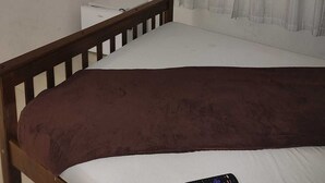 A bedroom with a single bed, a small bedside table, a TV mounted on the wall, and a window with sheer curtains. - Pousada Kasarão Praia Grande (Ubatuba)