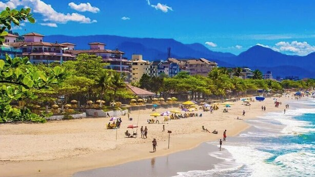 A beach with people, umbrellas, and buildings in the background. - Pousada Kasarão Praia Grande (Ubatuba)
