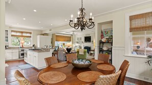 A spacious dining area with a large wooden table surrounded by wicker chairs, a chandelier, and a decorative bowl in the center. - Gated Seaside Community sleeps 10, private courtyard pool & community pool (St Simons Island)