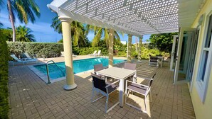 A pool area with a pergola, lounge chairs, and a table with chairs. - Waterfront Sanctuary Cove, 2Bed 2Bath, King Bed, Pool, Porch at Grand Harbour. (Grand Harbour)