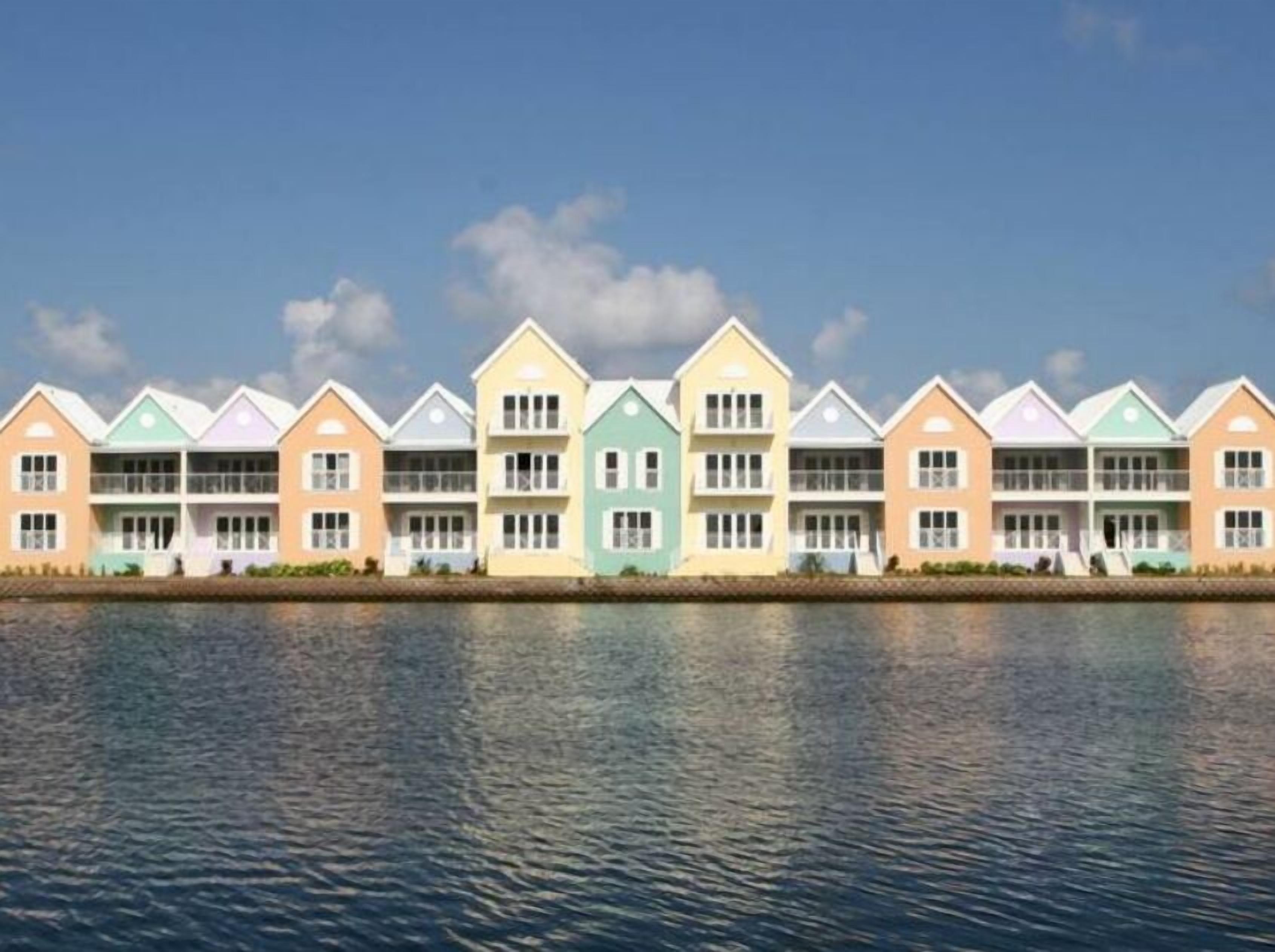 Eine Reihe farbenfroher, mehrstöckiger Gebäude mit Balkonen, vermutlich ein Hotel oder Resort, direkt an einem Gewässer gelegen.