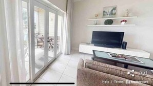 A modern living room with a sofa, a flat-screen TV, and a sliding glass door leading to an outdoor area. - Waterfront Sanctuary Cove, 2Bed 2Bath, King Bed, Pool, Porch at Grand Harbour. (Grand Harbour)