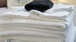 Une pile de serviettes blanches, soigneusement pliées, est posée sur un lit doté d’une tête de lit en bois et d’un oreiller orné d’un motif de lion.