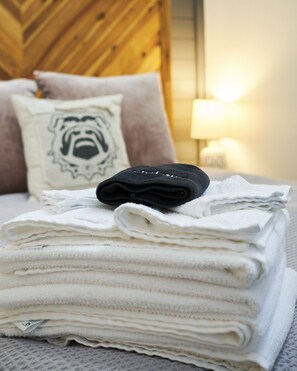 A neatly folded stack of white towels on a bed with a wooden headboard and a pillow with a lion design. - Iconic Downtown Athens Condo I Sanford Stadium View I 10 Min Walk to Games (Athens)