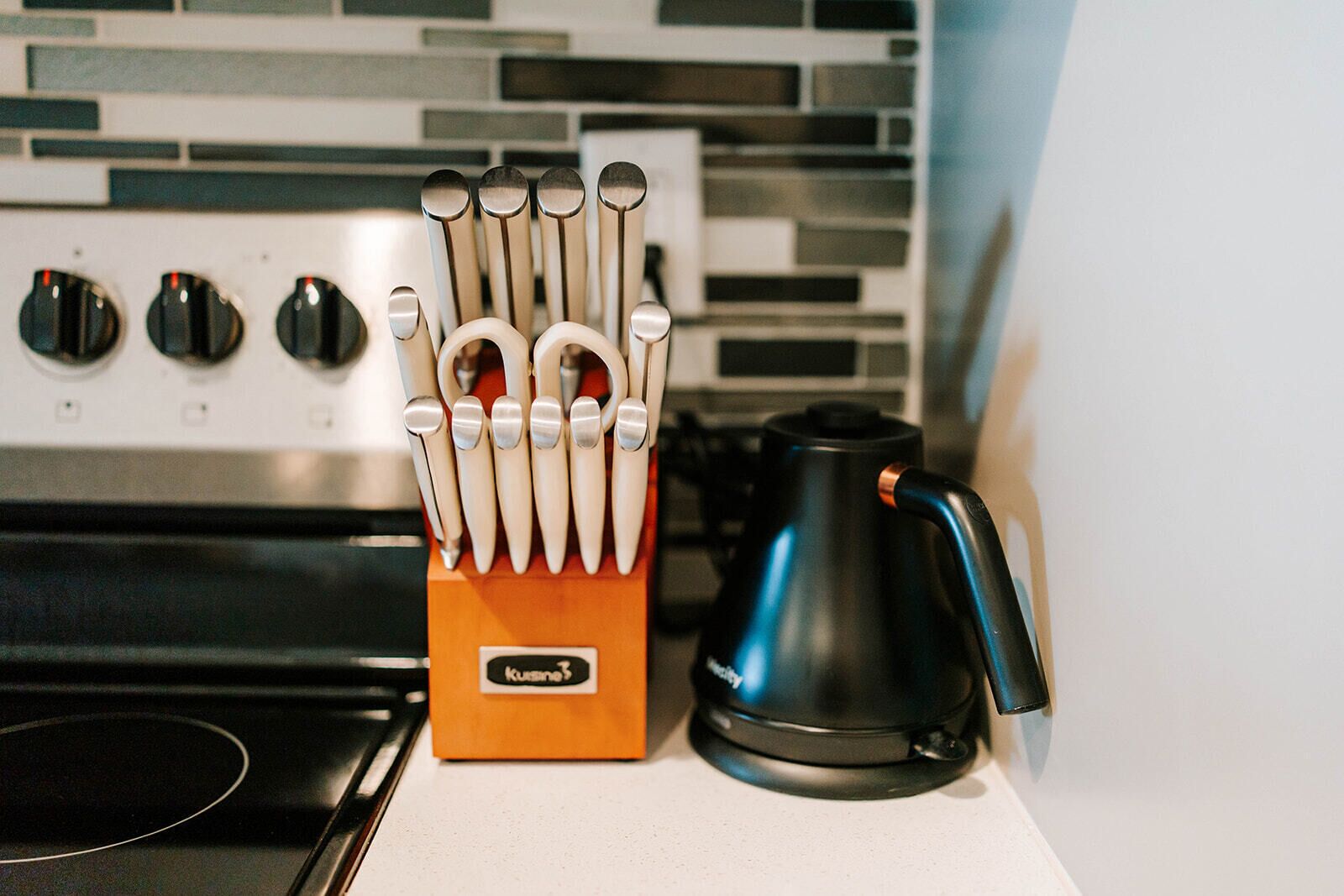 A kitchen with a utensil holder, a kettle, and a stove.