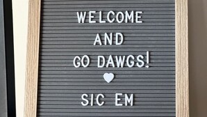 Une pancarte d’accueil encadrée, avec le texte « BIENVENUE ET ALLEZ, LES DAWGS ! » sur un fond texturé.