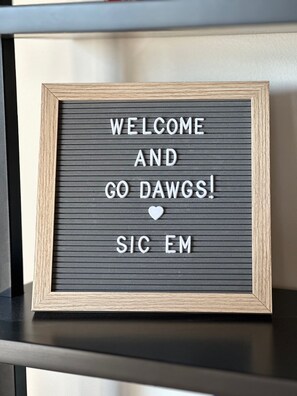 A framed welcome sign with the text "WELCOME AND GO DAWGS! SIC EM" on a textured background. - Iconic Downtown Athens Condo I Sanford Stadium View I 10 Min Walk to Games (Athens)