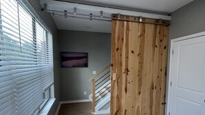 Un dormitorio con una cama, una puerta corredera de madera, una escalera y un ventanal con persianas.