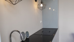 Une cuisine moderne dotée d’un plan de travail noir, d’un évier en acier inoxydable et d’une cuisinière encastrée. Deux suspensions lumineuses aux ampoules apparentes illuminent l ’espace.