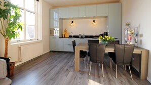 Une cuisine moderne avec des meubles blancs, une table à manger avec des chaises et une grande fenêtre agrémentée d’une plante.