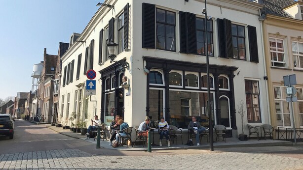 Une rue bordée d’immeubles traditionnels européens, dont certains abritent des boutiques au rez-de-chaussée. On y trouve des terrasses où les gens sont assis.