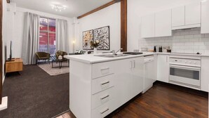 A modern kitchen with white cabinetry, a central island, and a built-in oven. - Heart of Darling Harbour (Pyrmont)