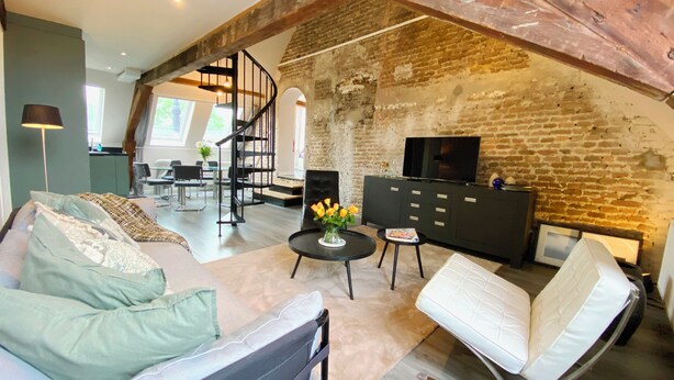 A spacious loft with exposed brick walls, a modern kitchen, a dining area, and a living room with a sofa and a TV. - Spacious cosy apartment in historic building in the centre of charming Vianen (Vianen)
