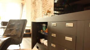 A modern living room with a leather chair, a dark wooden cabinet with drawers, and a brick wall. - Spacious cosy apartment in historic building in the centre of charming Vianen (Vianen)